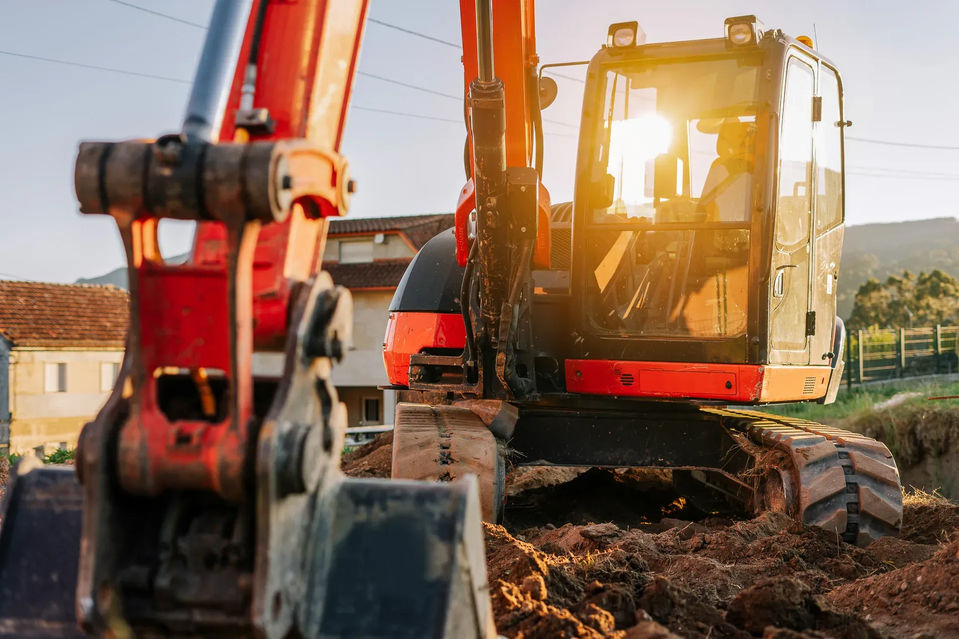 Bagger im Einsatz auf einer Baustelle im Wohngebiet bei Abendlicht